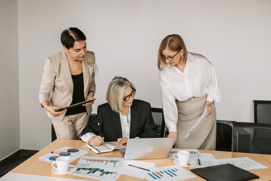 Three businesswomen discussing documents during a meeting in a modern office setting.